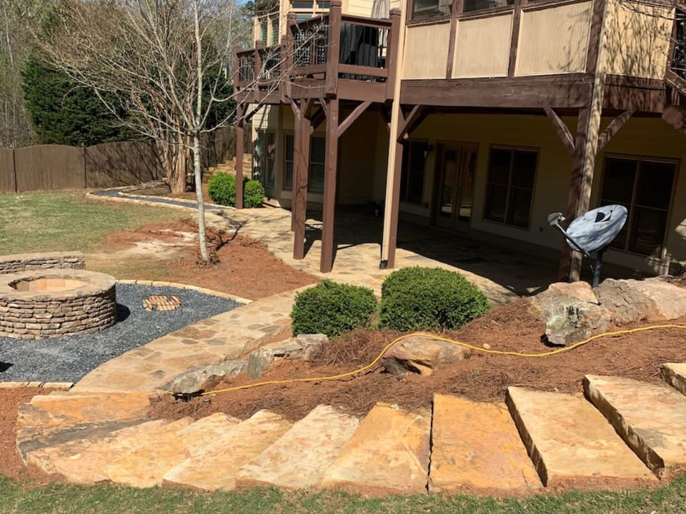 Wide flagstone steps leading to a stone fire pit on a gravel pad below a deck